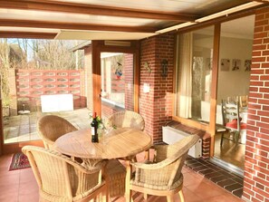 A patio with a round table and wicker chairs, a bottle of wine, and a glass on the table. - Haus Heike - Holiday Apartment Ground Floor (Utersum)