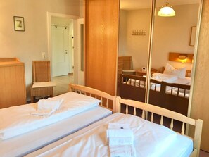 A hotel room with two single beds, a wooden headboard, a mirror, a small bedside table, a chair, and a wardrobe. - Haus Heike - Holiday Apartment Ground Floor (Utersum)