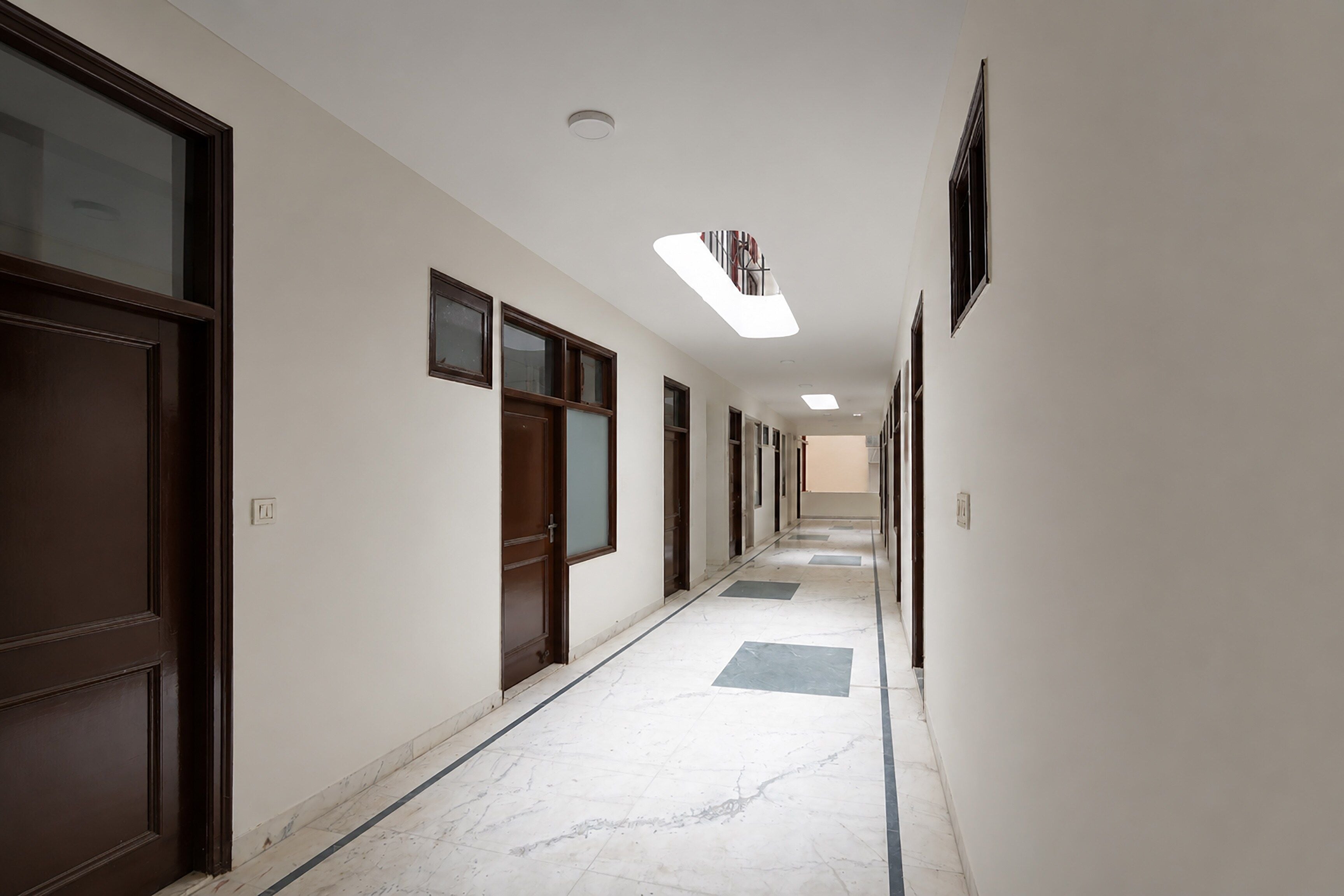 A long, narrow hallway with doors on both sides, a tiled floor, and a ceiling with recessed lighting.