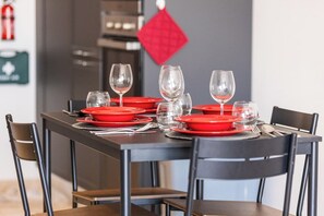 A dining table set with red plates and clear glasses, with a red diamond-shaped decoration on the wall behind. - Stay in this bright and modern 1-bedroom apartment in Marsaskala, Malta. Enjoy a spacious open-plan living area, fully equipped kitchen, air conditioning and a comfortable double bedroom, ideal for couples, solo travellers or longer stays. (Marsaskala)