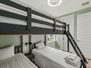 Une chambre avec un lit superposé, une échelle, une table de chevet et une petite table d’appoint.