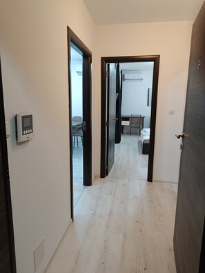 A hallway with a door leading to a room with a desk and chair, a small table with a chair, and a bed. - One-Bedroom Apartment-14 Filip Makedonski 49B (Plovdiv)