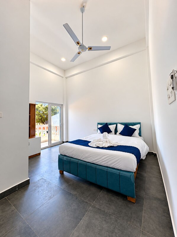 Un dormitorio moderno con una cama grande, un ventilador de techo y vistas al exterior a través de una puerta corrediza.