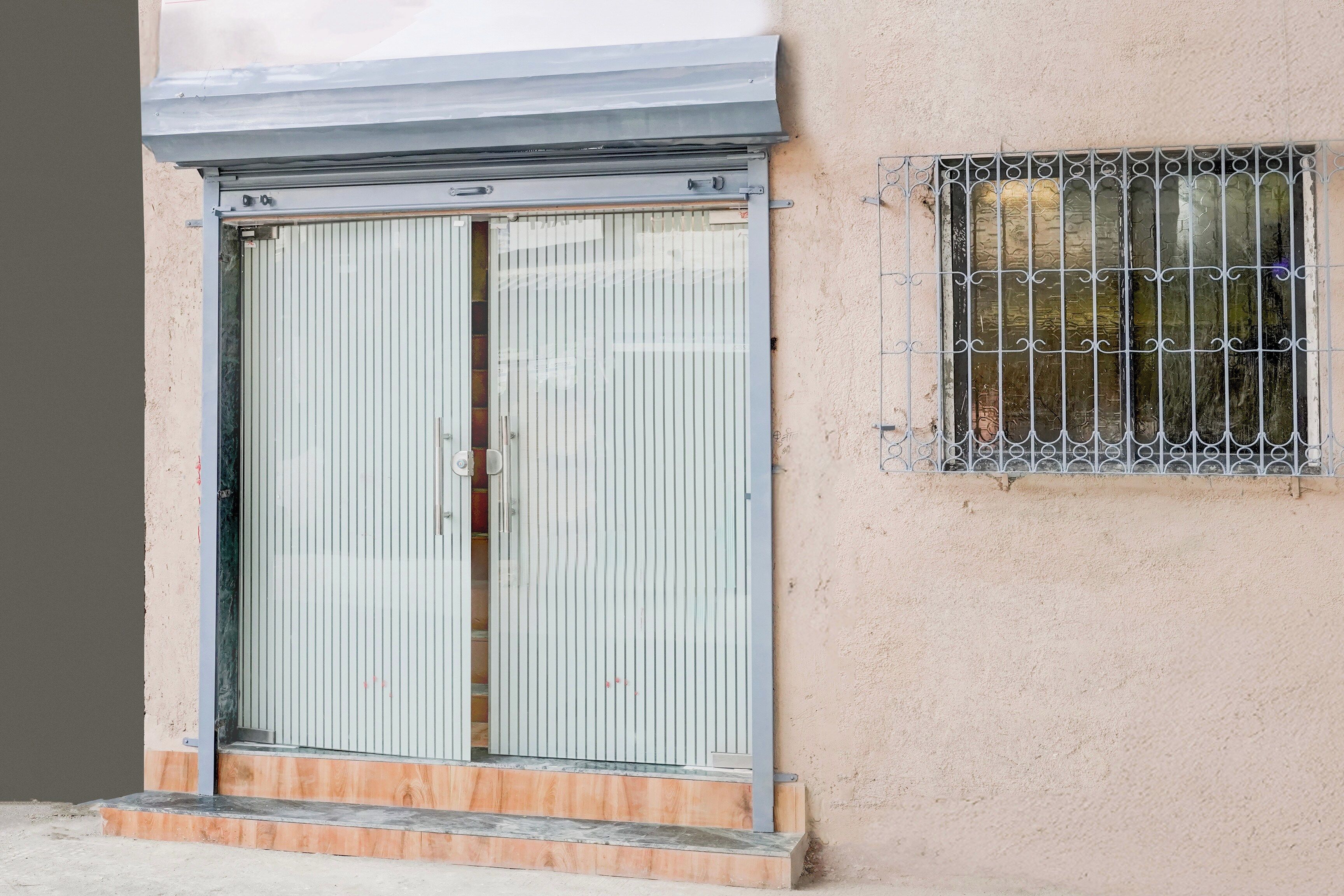 Un edificio con una puerta metálica grande y una ventana con barrotes.