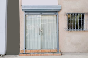 Una puerta metálica cerrada con un patrón de franjas verticales, una pequeña ventana con una reja de metal y un escalón de concreto que conduce a la puerta.