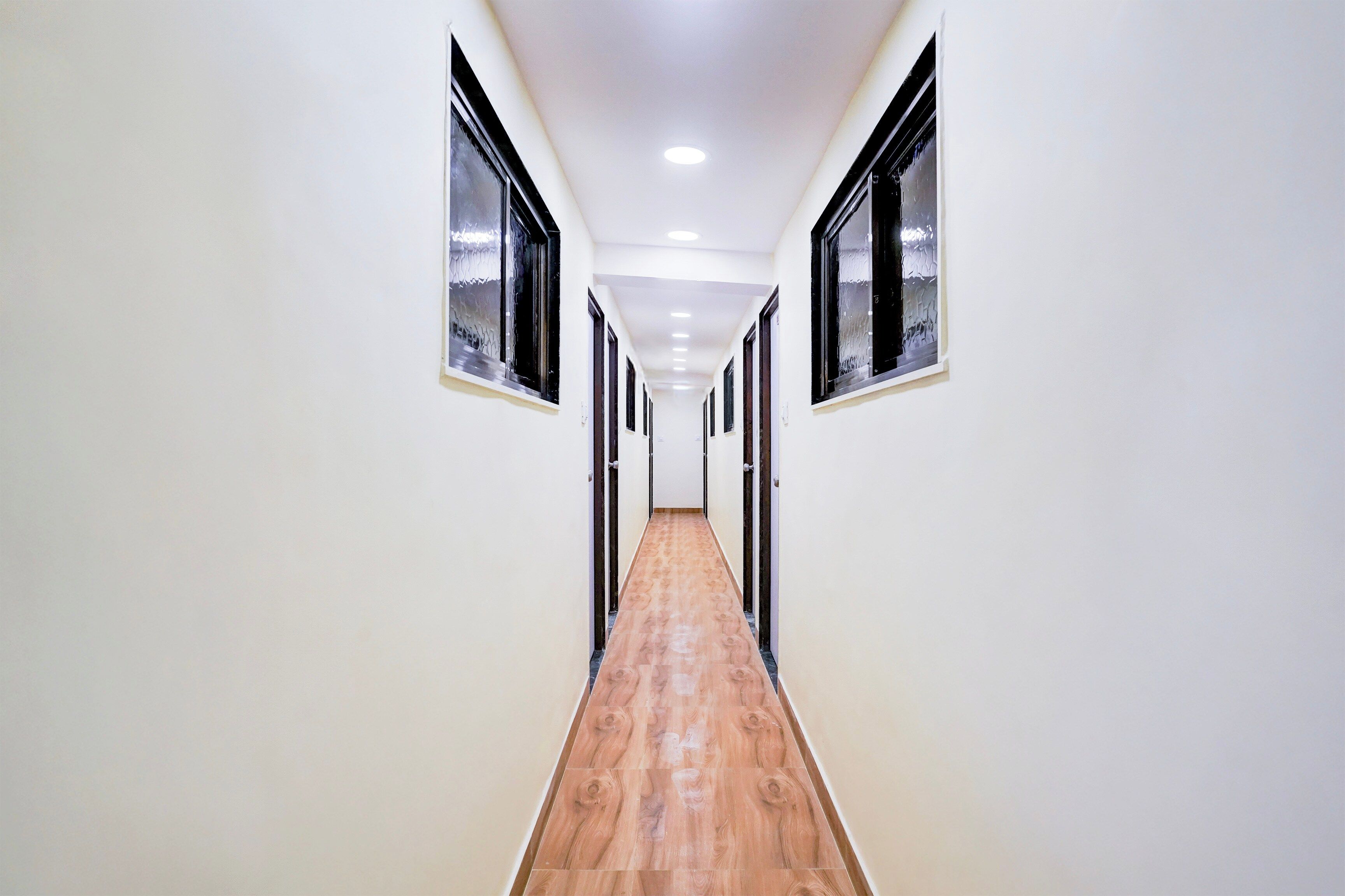 Un pasillo con paredes blancas, suelo de madera y ventanas de marco negro.