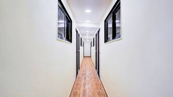 Un couloir aux murs blancs, au plancher en bois et aux fenêtres à cadre noir.