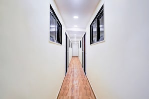 Un pasillo con paredes blancas, suelo de madera y ventanas de marco negro.