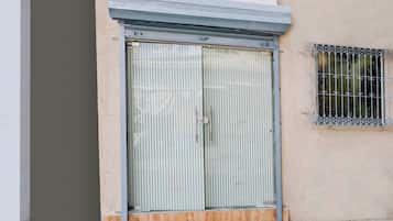 Une porte à deux battants avec des stores verticaux, une petite fenêtre ornée de barreaux décoratifs et une marche en béton menant à la porte.