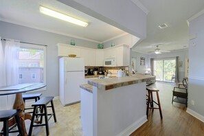 A modern kitchen with white cabinetry, a central island, and a dining area with a table and chairs. - Great Location! Kissimmee Condo 5 Mi to Disney (Kissimmee)