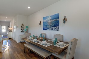 A dining area with a wooden table set for four, a bench, and a wall-mounted painting of a coastal scene. - 2 Mi to Panama City Beach: Modern Townhome (Panama City Beach)