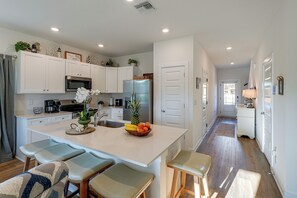 A modern kitchen with white cabinetry, a central island with bar stools, and a fruit bowl. - 2 Mi to Panama City Beach: Modern Townhome (Panama City Beach)