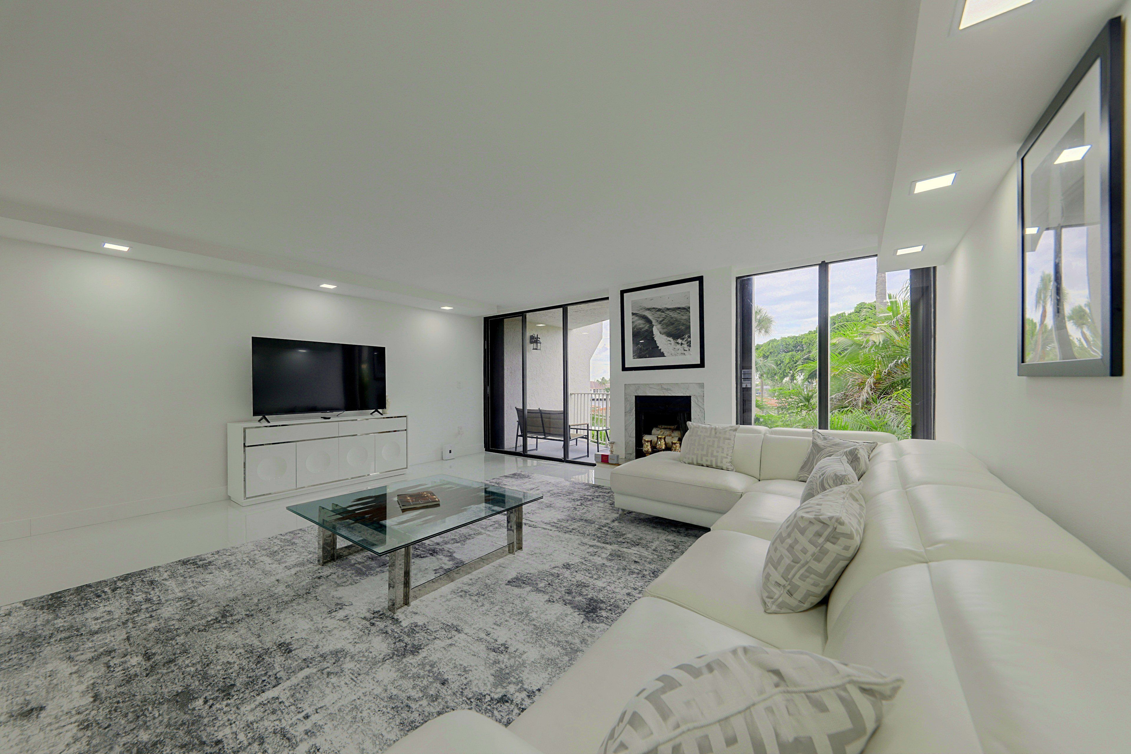 A modern living room with a flat-screen TV, a glass coffee table, a white sofa, and a fireplace.