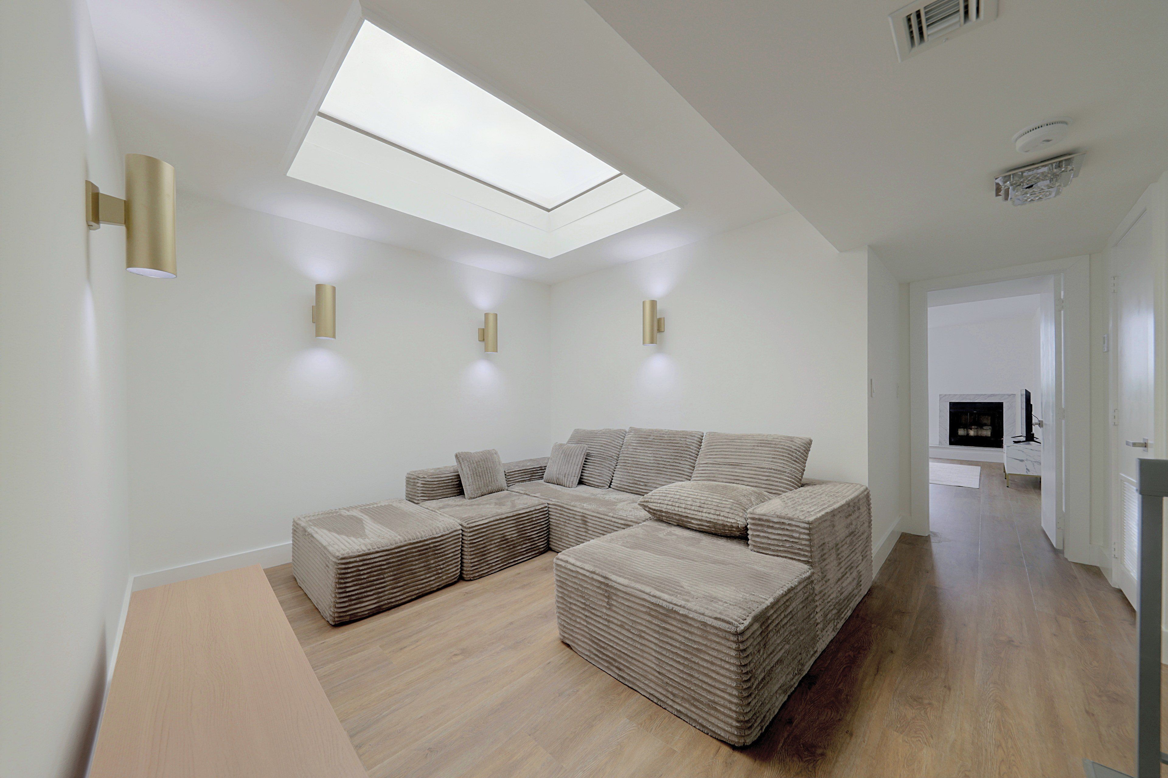 A modern living room with a sectional sofa, a skylight, and built-in wall sconces.