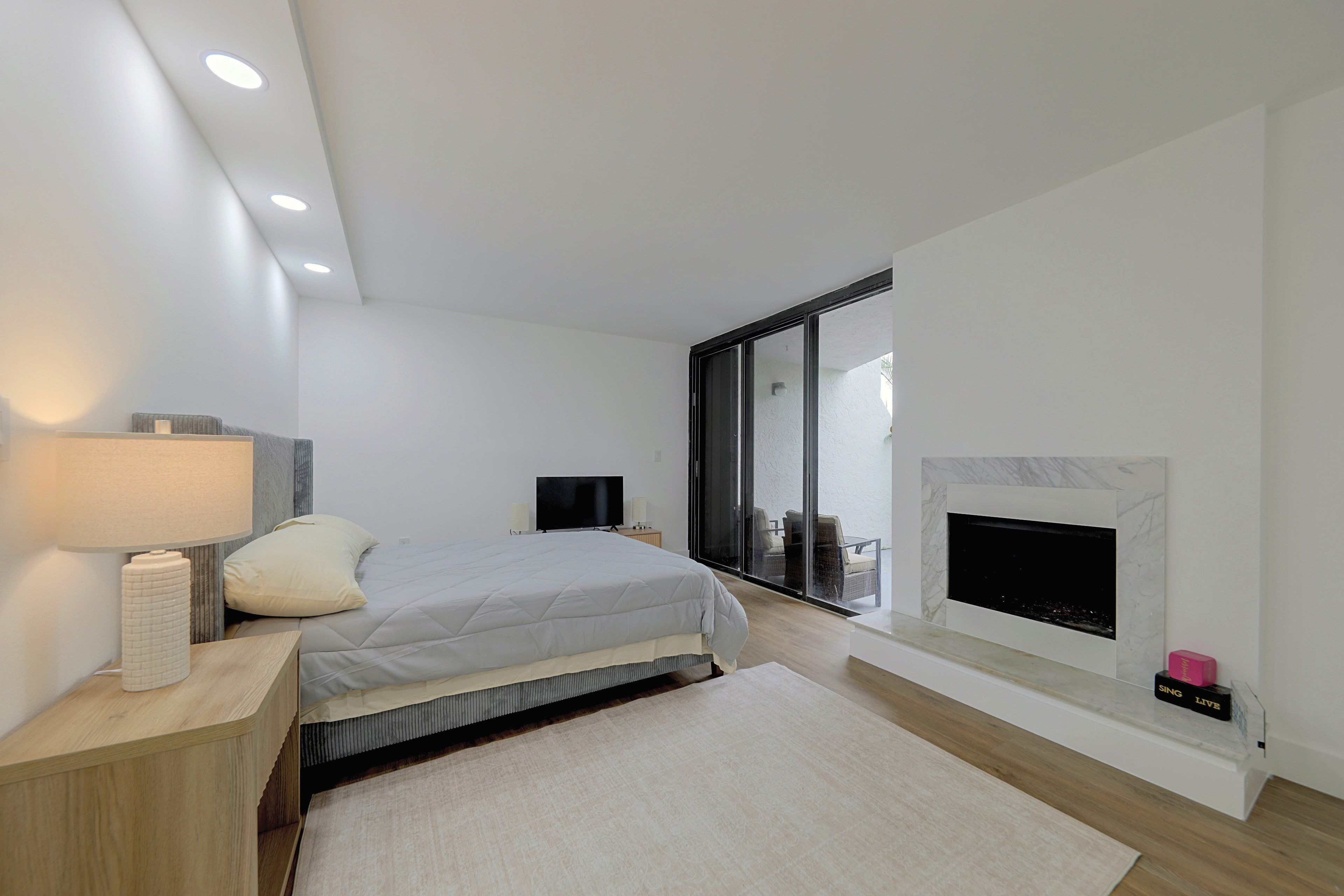 A modern bedroom with a bed, bedside lamp, TV, and a fireplace.