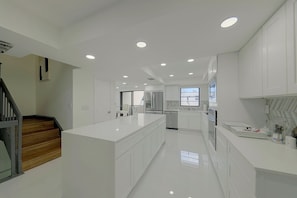 A modern kitchen with white cabinetry, a central island, and recessed ceiling lights. - Relax Poolside, Walk to Ocean! Hillsboro Beach Gem (Hillsboro Beach)