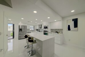 A modern kitchen with a central island, stainless steel appliances, and a herringbone-patterned backsplash. - Relax Poolside, Walk to Ocean! Hillsboro Beach Gem (Hillsboro Beach)
