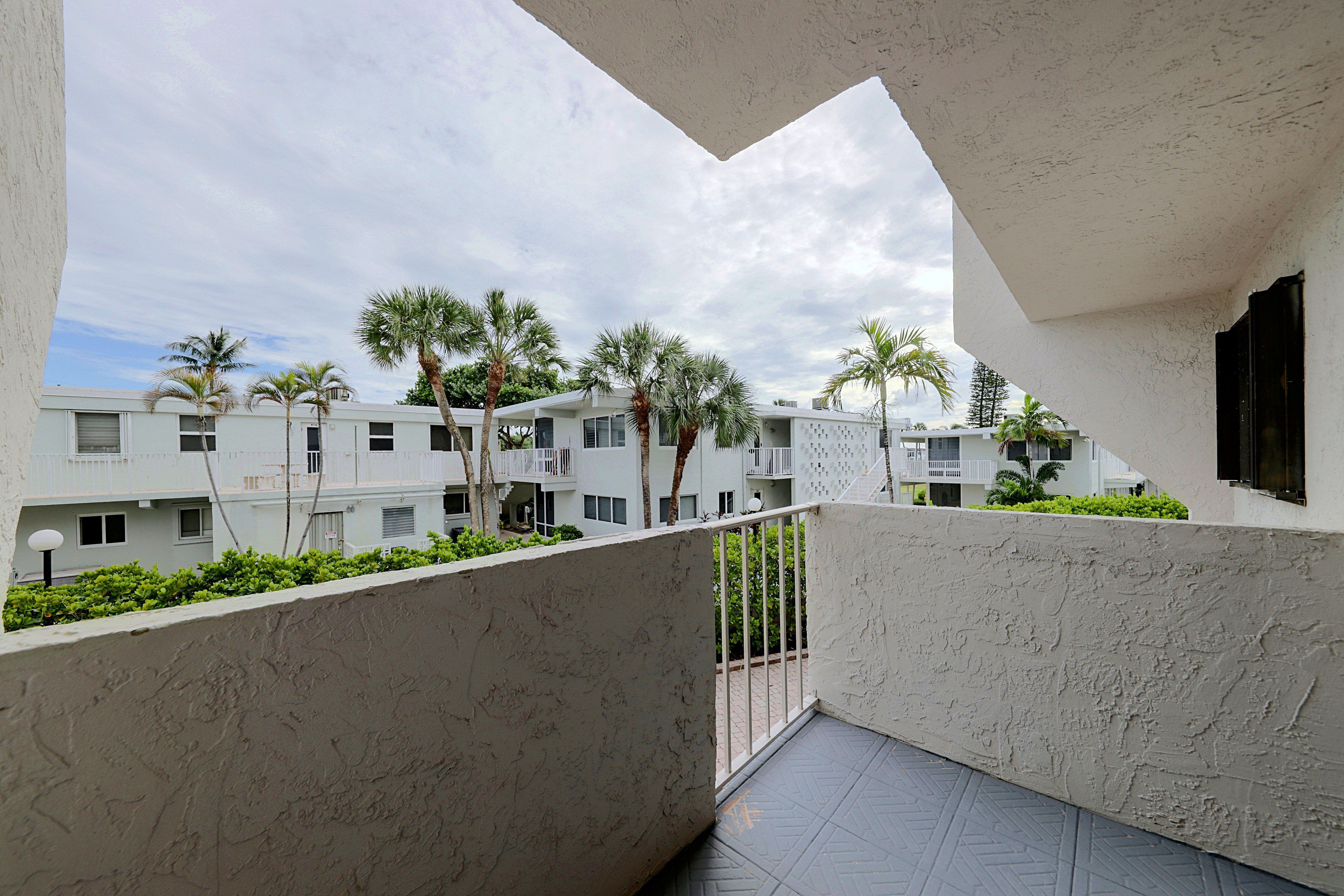 A residential building with a balcony, white exterior walls, and palm trees.