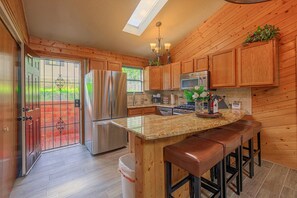 A kitchen with wooden cabinets, stainless steel appliances, a granite countertop, and a bar stool area. - Walk to Midtown! Family Getaway w/ Wraparound Deck (Ruidoso)