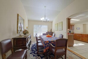 Comedor con una mesa dispuesta para cuatro, sillas a cada lado, una lámpara de cristal y un espejo grande en la pared.
