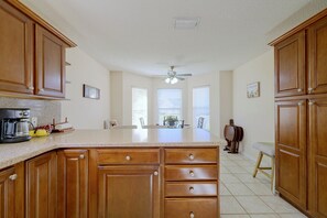 Cocina con gabinetes de madera, una encimera, un ventilador de techo y una zona de comedor con mesa y sillas.