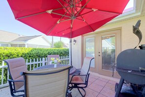 Un patio al aire libre con una sombrilla roja, una parrilla y una mesa con sillas.