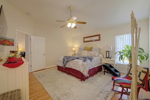 A bedroom with a bed, a ceiling fan, a nightstand, a lamp, a window with blinds, a potted plant, and a chair. - 3 Mi to Spanish Springs! Peaceful Retreat (Lady Lake)