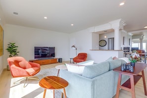 A modern living room with a large sofa, a television, and a dining area with a table and chairs. - Your Oceanfront Home Away From Home in Long Beach (Long Beach)