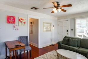 A living room with a ceiling fan, a green sofa, a wooden table, and artwork on the walls. - Walk to Pickleball, Parks, Pubs! Cozy Dtwn Apt (Bakersfield)