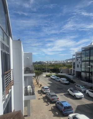 A parking lot with multiple cars, a building with a balcony, and a clear sky. - Lovely 2-bedroom apartment in Big Bay for a relaxing stay (Cape Town)