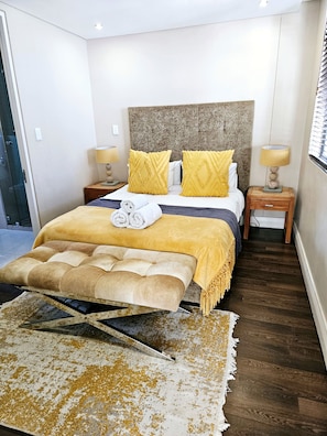 A bedroom with a bed, two bedside tables, a headboard, a rug, and a door. - Lovely 2-bedroom apartment in Big Bay for a relaxing stay (Cape Town)
