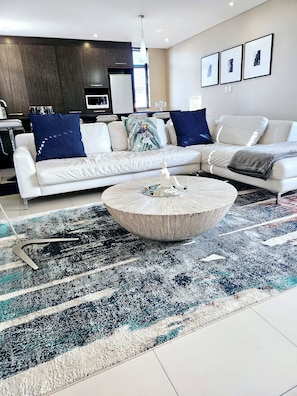 Ein modernes Wohnzimmer mit einem weißen Sofa, einem runden Couchtisch und einem gemusterten Teppich.