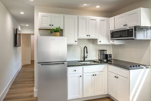 Una cocina moderna con armarios blancos, un refrigerador de acero inoxidable, un microondas y una cafetera.