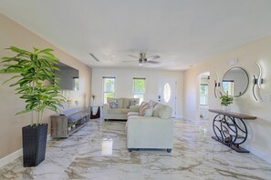 A spacious living room with a marble floor, a sofa, a coffee table, and a large potted plant. - Right on Canal! Sleek Home Near Gulf Coast Fun (Hudson)