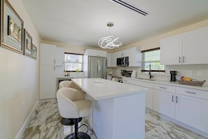 A modern kitchen with white cabinetry, a marble floor, a central island with bar stools, and a pendant light. - Right on Canal! Sleek Home Near Gulf Coast Fun (Hudson)