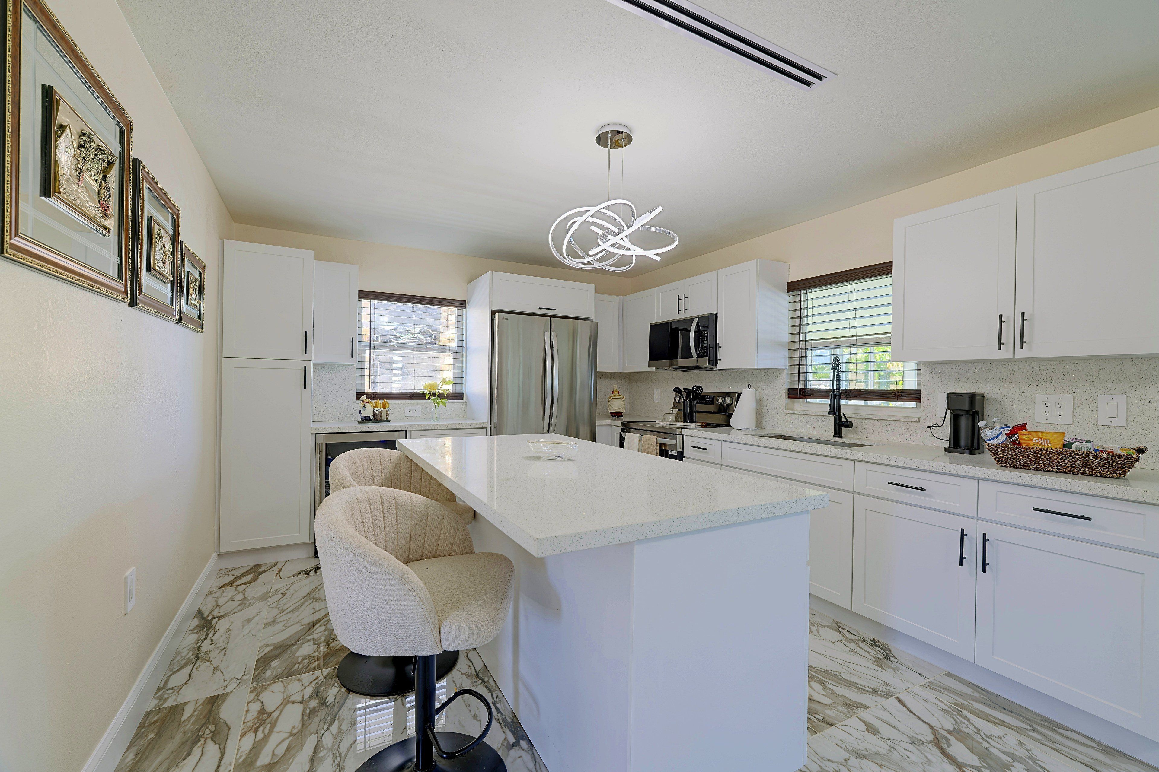 A modern kitchen with white cabinetry, a marble floor, a central island with bar stools, and a pendant light.