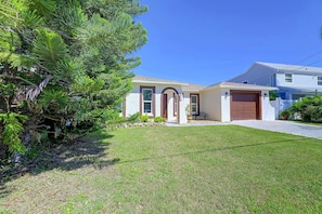 A residential house with a well-maintained lawn, a garage, and a large tree in the front yard. - Right on Canal! Sleek Home Near Gulf Coast Fun (Hudson)