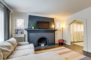 A living room with a fireplace, a sofa, a television, and a lamp. - Historic Detroit Charm Near Area Hospitals (Detroit)