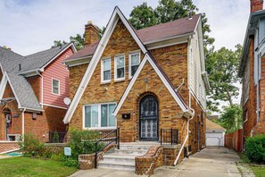 A two-story brick house with a gabled roof, a front door with decorative ironwork, and a small front porch with steps. - Historic Detroit Charm Near Area Hospitals (Detroit)