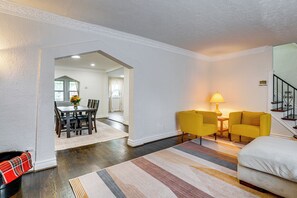 A living room with a sofa, a coffee table, and a lamp. There is a dining area with a table and chairs. The room has hardwood flooring and white walls. - Historic Detroit Charm Near Area Hospitals (Detroit)