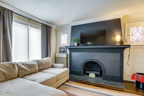 A living room with a fireplace, a sofa, and a television. - Historic Detroit Charm Near Area Hospitals (Detroit)