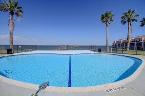 A clear blue swimming pool with a 4 ft depth marker, surrounded by palm trees and a fence. - Aransas Bayfront, Fishing Pier and Boat Ramp (Rockport)