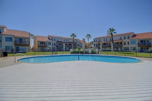 A swimming pool surrounded by a wooden deck, with apartment buildings in the background. - Aransas Bayfront, Fishing Pier and Boat Ramp (Rockport)