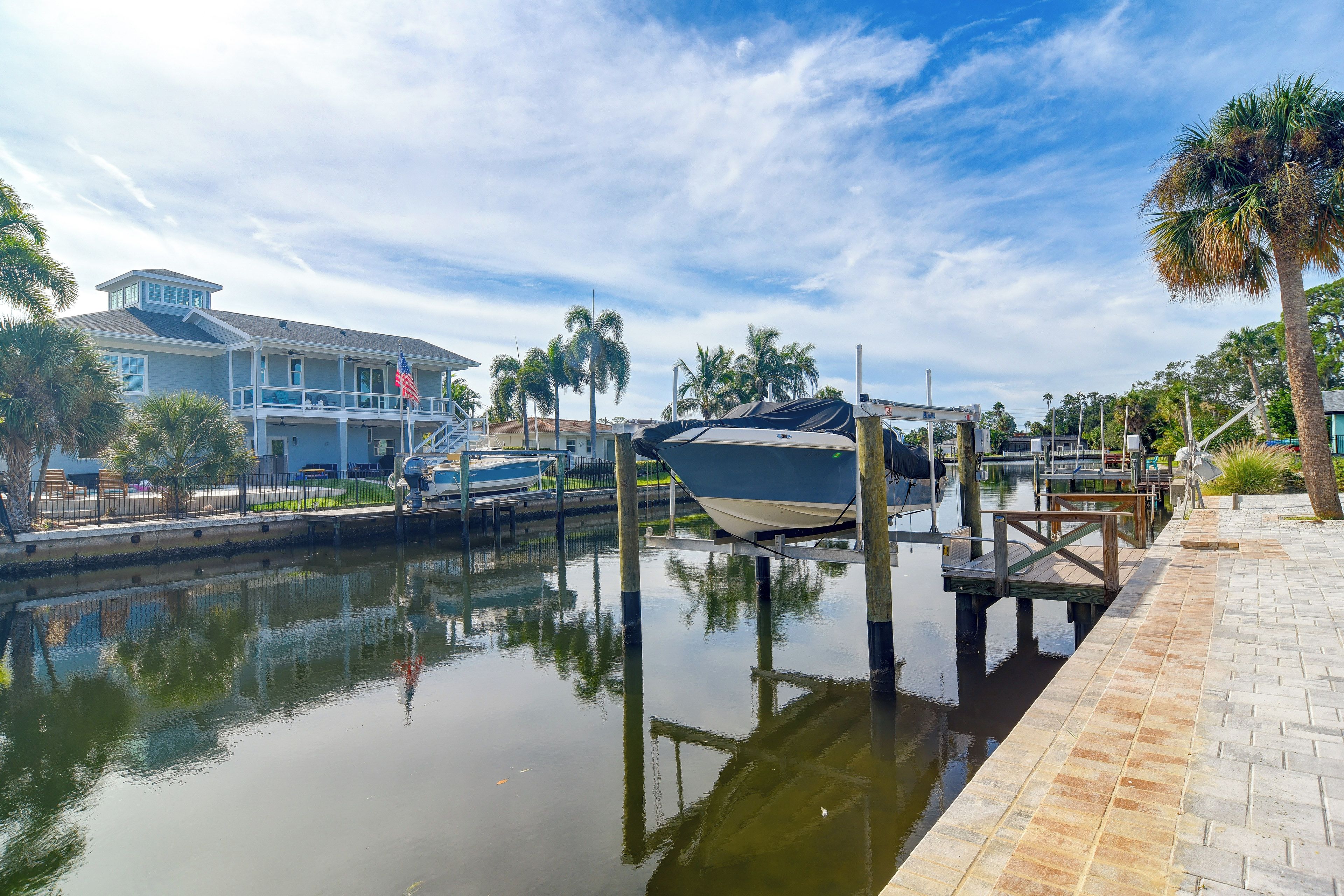 A marina with boats docked, a house with a balcony, and palm trees.