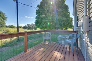 A wooden deck with a metal fence, two white plastic chairs, and a large tree in the background.