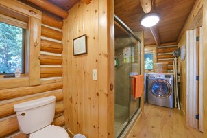 Un baño de cabaña de madera con inodoro, un cuadro enmarcado, lavadora y zona de ducha.