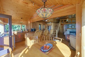 A wooden cabin interior with a dining area, kitchen, and a staircase leading to a loft. - Waterfront Lake Charlevoix Cabin 8 Mi to Boyne Mtn (Boyne City)