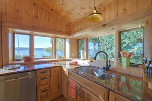 A kitchen with wooden cabinets, a granite countertop, a sink, and large windows offering a view of the outdoors. - Waterfront Lake Charlevoix Cabin 8 Mi to Boyne Mtn (Boyne City)
