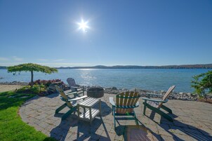 Un patio frente al agua con sillas Adirondack y una chimenea.