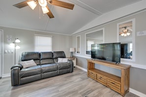 A living room with a leather sofa, wooden entertainment unit, ceiling fan, and a large flat-screen TV. - Countryside Gem w/ Fire Pit: 14 Mi to Mammoth Cave (Brownsville)